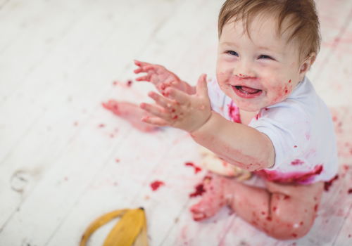 Young baby playing on floor messy with food or paint