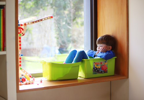 Young child sitting in buckets on window ledge, waiting
