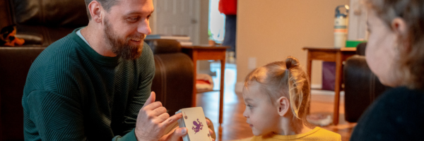 Father and young daughters sitting on the floor doing flip cards or leaning letters, sounds and colors