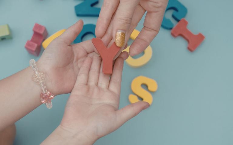 Adult hands pass an alphabet letter to a child during a learning activity.
