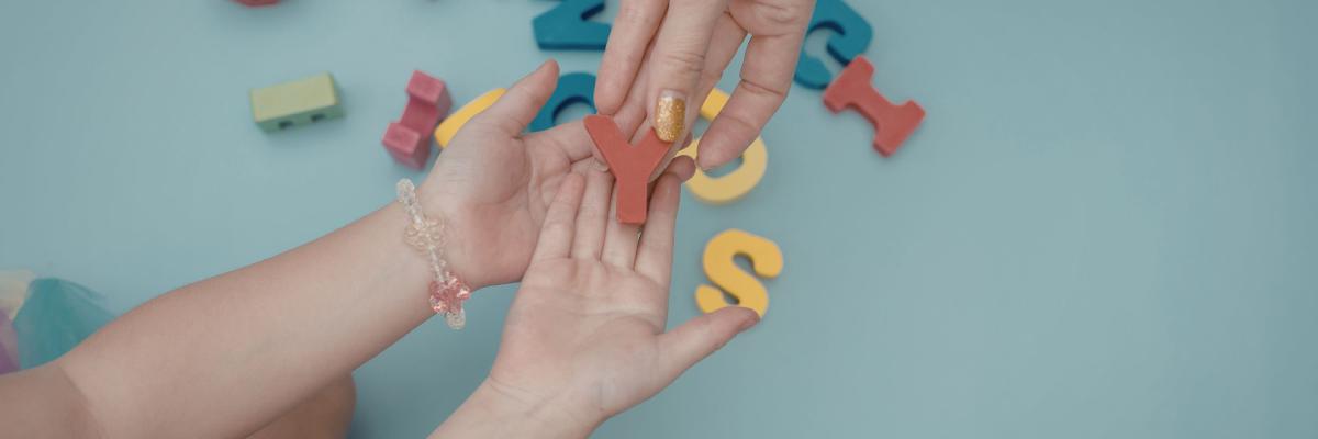 Adult hands pass an alphabet letter to a child during a learning activity.