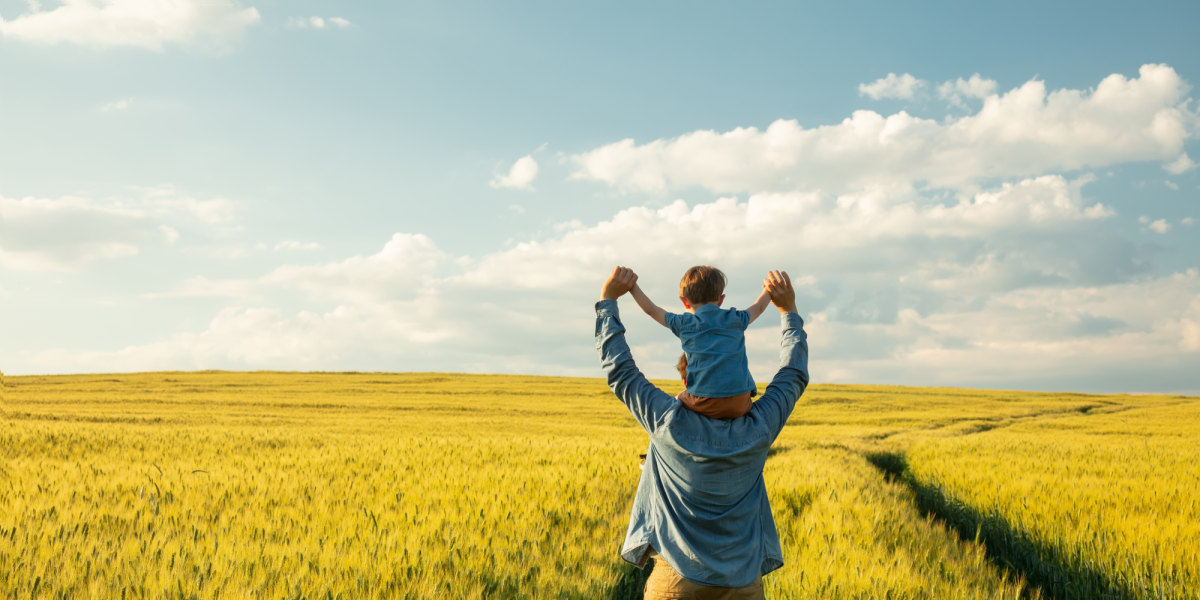 Caregiver and child walking through a field with their arms in the air. 